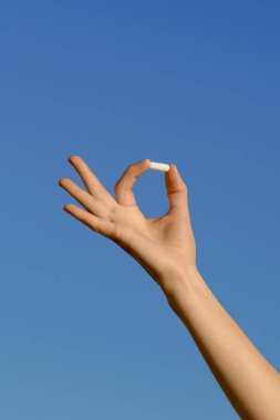 Mavi izole bir arka planda parmaklarıyla hap tutan bir kadının dikey görüntüsü. Doğal beslenme takviyeleri, ilaç ve eczane kavramı, sağlık hizmetleri