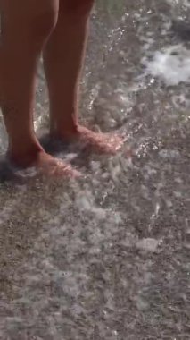 Genç bir kadının ayaklarının denizin kumu üzerinde durduğu ve suyla yıkandığı dikey bir video. Tatildeki gerçek insanlar kavramı, kullanıcı içeriği, yaz eğlencesi, ayak masajı