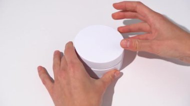Kadın elleri pembe bantlı beyaz bir kavanozu açar, beyaz masa arkasında bir spatula çıkarır. Gözlerin altındaki güzellik ürünleri kavramı koyu halkalar, pürüzsüz kırışıklıklar, nemlendirici..