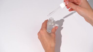 Kadın elleri serumun cam kavanozunu açar ve avucunun içinde pipet kutusuyla uygular ve beyaz izole masa arkaplanına sürter. Cilt besin, su ve güzellik ürünleri konsepti