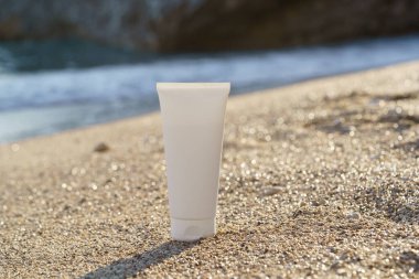 Sahildeki denizin arka planında ıslak kumun üzerine beyaz krem tüpü. Güneş ve morötesi koruma, nemlendirici ve cilt bakımı, güzellik ve estetik kavramı.