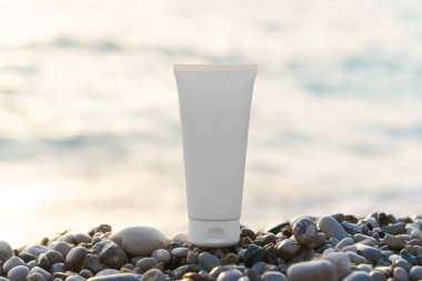 Deriyi nemlendirmek ve denizin arka planına karşı çakıl taşlarının üzerindeki güneşten korumak için beyaz mocap krem tüpü. Güzellik ürünleri, yüz ve vücut bakımı, güneş kremi