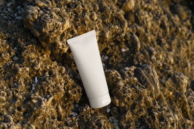 Denize yakın kayaların üzerindeki beyaz krema tüpünün yan görüntüsü. Güzellik ürünleri, doğal yüz ve vücut bakımı, güneş kremi ve korunma kavramı