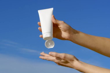 Dişi eller, mavi bir arka planda parmağına beyaz bir krem tüpü sıkıyor. Vücut ve yüz bakımı için doğal ürünler kavramı. Tasarımın için resim