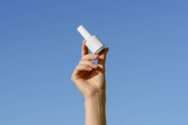 Beyaz, boş, tırnak cilası dolu bir kavanoz tutan bir kadın eli ya da parmakları mavi, izole bir arka planda olan bir jel. Güzellik ve estetik ürünleri kavramı, tırnak tasarımı, güzellik salonları