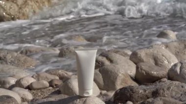 Beyaz krema tüpü, deniz dalgaları ve çakıl taşlarının arka planında. Güneş kremi ve nemlendirici kozmetik konsepti, güneşten koruma