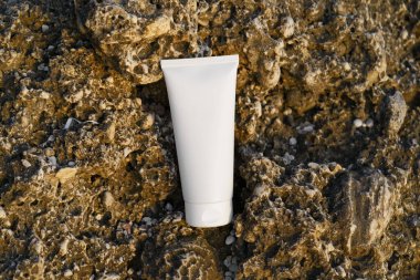 Sahildeki deniz kenarındaki kayanın üzerinde beyaz bir krema tüpü. Doğal güzellik ürünleri, yüz ve vücut bakımı, güneş kremi ve güneş koruması kavramı
