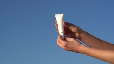 Kadın elleri mavi arka planda serum ya da krem ile beyaz model tüp açar. Yüz bakımı için doğal kozmetik kavramı SPF, cilt koruması ve hidrasyon.