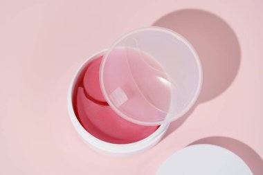 Pembe hidrojel bantlı beyaz kavanoz ve pembe izole edilmiş arka planda spatula ile şeffaf bir kapak. Kurumayla savaşır, kırışıklıkları azaltır, deriyi sıkılaştırır ve göz altı karanlık kavramını en aza indirir.