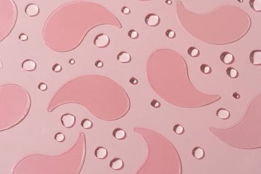 Pembe hidrojel göz bantları ince bir damla dokusuyla pembe bir yüzeye kurulmuş. Göz altı bölgesini nemlendirmek, pürüzsüz ve tazelemek için tasarlanmış günlük cilt bakımı ritüelleri..