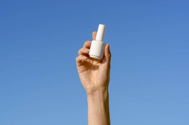 Mavi arka planda beyaz, boş, tırnak cilası dolu bir kavanoz tutan bir kadın. Güzellik ürünleri, jöle parlatıcıları, güzellik salonları. Tasarımın için bir model