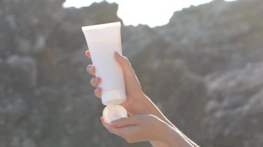 Kadın eller beyaz bir model tüp açar ve güneş ışığıyla aydınlatılmış bir kaya zeminine krem sürerler. Cilt bakımı, güzellik ve estetik için doğal kozmetik kavramı. Kullanıcı tarafından oluşturulan içerik