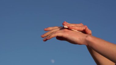 Kadın eli, mavi gökyüzü arka planına nemlendirici sürüp sürterek nemlendirir. Güzellik ve vücut bakım ürünleri kavramı, doğal kozmetik ürünleri.