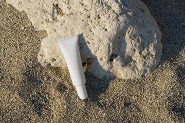 Kıyıdaki kumların üzerinde ince beyaz bir krem tüpü ya da serum. Güzellik ürünleri, gözün etrafındaki yüz ve cilde dikkat edin, yaşlanma önleyici ve kırışıklık önleyici etki.