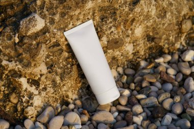 Sahilde deniz kenarındaki kireçtaşı kayanın üzerinde duran beyaz krema tüpü. Doğal güzellik ürünleri, yüz ve vücut bakımı, güneş kremi ve güneş koruması kavramı