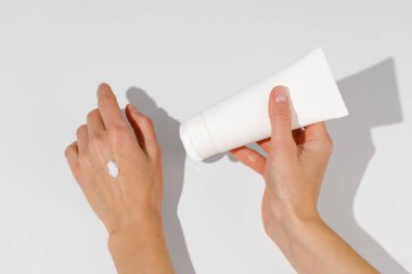 Cildinde doku örneği olan kadın eller beyaz izole arka planda beyaz mokap boş tüp kremi tutuyor. Yüz bakımı, besin, nemlendirici ve güneş koruması kavramı.