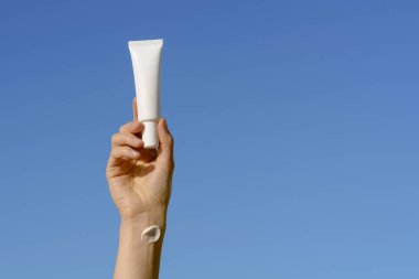 Cildinde krem lekesi olan kadın eli mavi arka planda beyaz krem ya da serum tutuyor. Yüz bakımı kavramı, estetik ürünler. Tasarım veya metin için yer