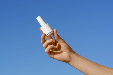 Beyaz tırnak cilası kavanozu ya da mavi izole gökyüzü arka planında jöle tutan kadın eli. Güzellik ve estetik ürünleri kavramı, tırnak tasarımı, manikür güzellik salonları.