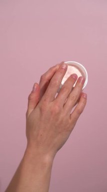 Beyaz maket kavanozundan krem alıp pembe izole arka planda cilde sürttüğü dikey video. Güzellik ürünleri, yüz ve vücut bakımı, beslenme ve hidrasyon kavramı