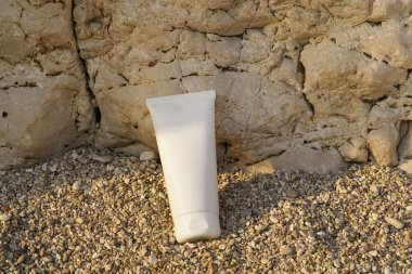 Kayadan bir arka planda küçük bir çakıl taşı üzerinde beyaz bir krem tüpü. Güzellik, vücut ve yüz bakım ürünleri kavramı. Tasarımın için resim