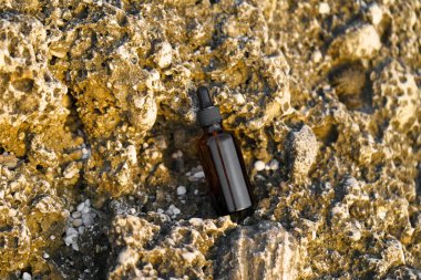 Deniz kenarındaki kireçtaşı kayanın üzerinde kahverengi serum kavanozu modeli. Cilt bakımı ve restorasyonu için doğal kozmetik ürünleri, kırışıklık azaltma, hidrasyon ve parlaklık.
