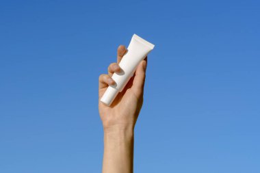 Mavi arka planda beyaz krem tüpünü tutan bir kadın. SPF ve güzellik ürünleriyle yüz ve göz bakım kozmetiği kavramı. Tasarımın için resim