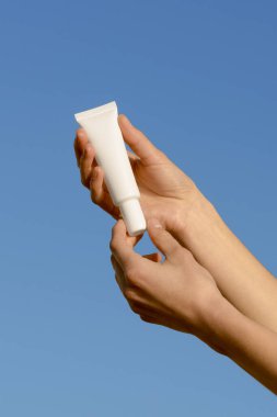 Mavi arka planda beyaz krem tüpünü tutan kadınların dikey görüntüsü. Güzellik ürünleri, yüz ve vücut bakımı kavramı. Tasarımın için resim