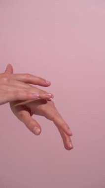 Pembe izole arka planda cilde sürtünen ve masaj yapan kadın ellerinin dikey videosu. Güzellik ürünleri, vücut bakımı, beslenme ve su tüketimi kavramı