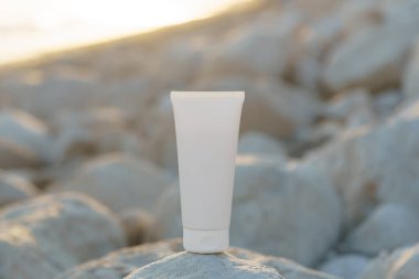 Sahildeki deniz kenarındaki çakıl taşları üzerinde batan güneş tarafından aydınlatılmış beyaz model krem. Güzellik ürünleri, vücut ve cilt bakımı, güneş koruması ve nemlendirici kavramı. Tasarımın için resim