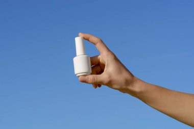 Mavi arka planda beyaz bir tırnak cilası kavanozu tutan kadın eller. Güzellik ürünleri, jöle cilası, manikür salonu, reklam.