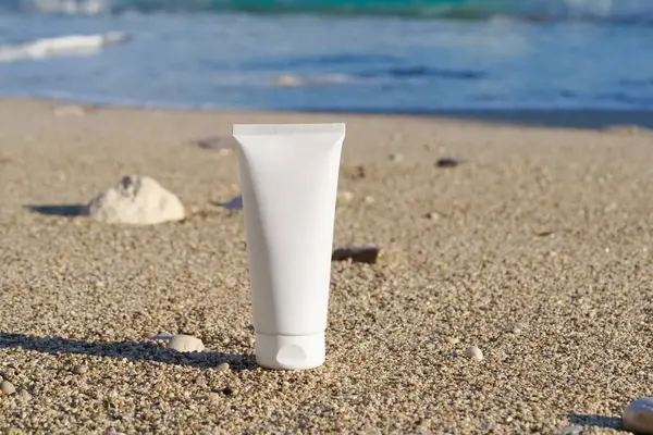 Sahildeki denizin arka planında ıslak kumun üzerine beyaz güneş kremi tüpü. Güzellik ve estetik, güneş koruması ve vücut için doğal kozmetik ürünleri, saç ve yüz bakımı.