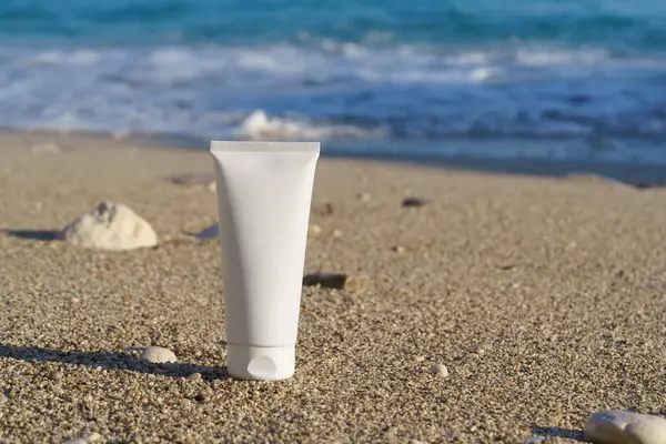 Sahildeki denizin arka planında ıslak kumun üzerine beyaz krem tüpü. Güneş koruması için doğal kozmetik ürünler, ultraviyole blok, cilt bakımı, güzellik ve estetik.