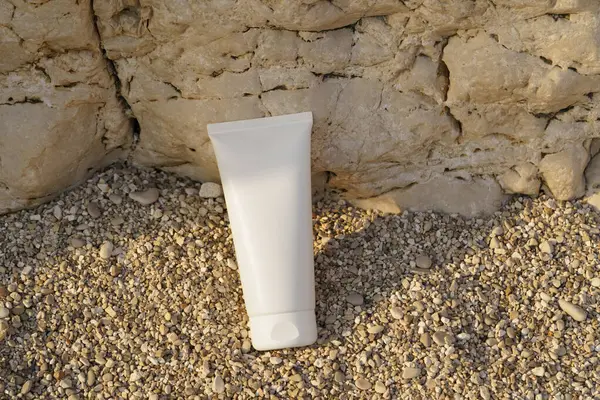 Kayadan bir arka planda küçük bir çakıl taşı üzerinde beyaz bir krem tüpü. Güzellik, vücut ve yüz bakım ürünleri kavramı. Tasarımın için resim