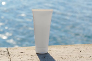Kayalık bir sahilde, deniz altyapısı olan basit beyaz bir krem tüpünün maketi. SPF kremi, cilt losyonu ya da minimalist güzellik kozmetik markası tanıtımı..