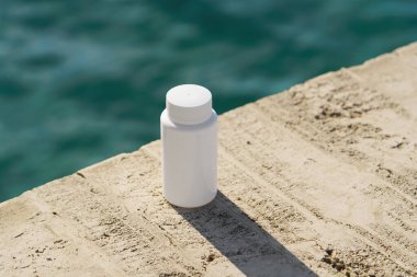 Deniz arka planında deniz kenarındaki kayalara yerleştirilmiş tabletli beyaz model konteynır. Doğal iyileşme, beslenme desteği, eczane, temiz sağlık konsepti..