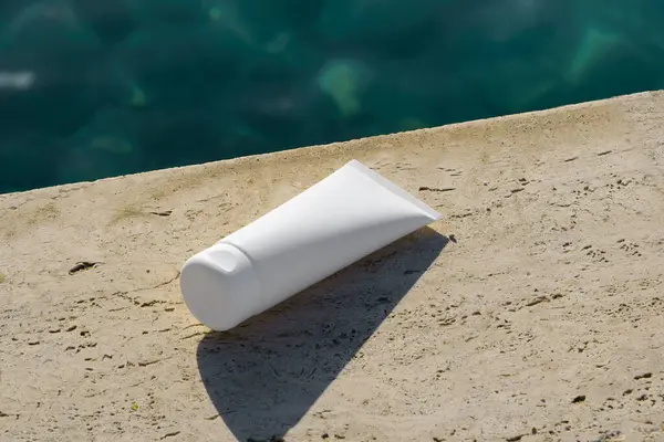 Sahildeki kayalıklarda duran, deniz altyapısı olan sahte beyaz kozmetik krem. Doğal güzellik ürünü reklamları için mükemmel, spf ile güneş kremi, ya da yüz nemlendirici markalaşma.