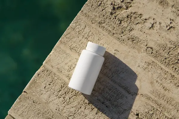 Deniz kenarındaki kayalarda duran haplarla dolu beyaz bir kavanoz. Doğadan esinlenilmiş sağlık hizmetleri, bitkisel takviyeler, sağlık yaşam tarzı, temiz tıp konsepti.