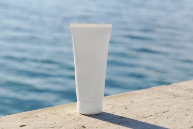 Arka planda deniz olan kayaların üzerine yerleştirilmiş beyaz kozmetik tüp. Güneş korumasını spf, yüz kremi ya da eko güzellik ürünleriyle desteklemek için mükemmel..