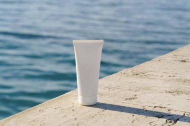 Okyanus kenarındaki beyaz kozmetik tüpün minimalist bir kopyası. Güneş kremi, gündüz kremi veya spf ile organik cilt güzellik ürünleri için doğal ışık ve deniz ayarı.