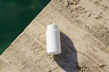 Deniz zemininde taşlı tabletlerin olduğu beyaz maket şişesi. Doğal ilaçların, diyet takviyelerinin, bütünsel sağlık hizmetlerinin, ilaç konseptinin sembolü..