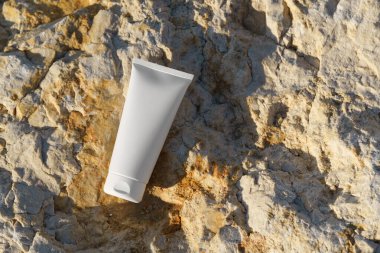 Deniz kenarındaki taşlara yerleştirilmiş beyaz bir kozmetik tüpün kopyası. Vücut bakımı, güneş koruması, yüz kremi ya da doğal güzellik ürünü reklamı kavramı.