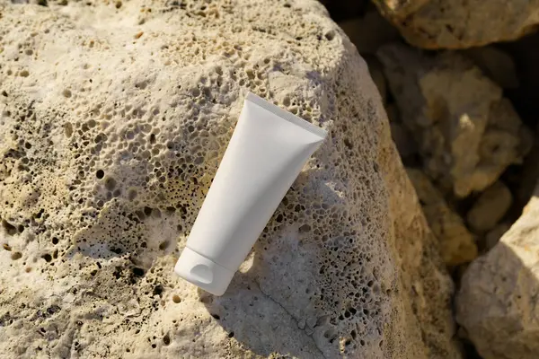 Deniz kenarındaki bir taşın üzerinde beyaz bir krem tüpü. Yüz ve vücut bakımı için doğal kozmetik kavramı güzellik ürünleri, güneş koruması. Tasarımın için resim.