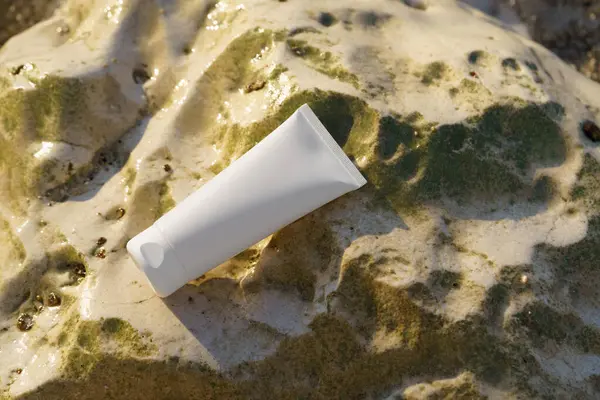 Beyaz cilt kremi tüpü ya da deniz suyunun yanındaki taşın üzerindeki losyon. Güzellik ve estetik kavramı, nemlendirici ve cilt bakım ürünleri, güneş kremi