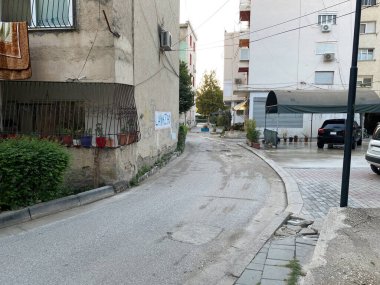 Sokak manzaralı, kır evleri, elektrik hatları ve doğal çevreye sahip geleneksel Arnavut mahallesi. Seyahat dergileri veya bölgesel hikaye anlatımı için ideal.