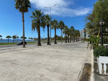 Vlora, Arnavutluk - 16 Ocak 2025: Akdeniz kıyı kasabasındaki palmiye ağaçları ve deniz manzaralı geniş cadde manzarası. Rahatlamış atmosfer seyahat, tatil ve sıcak tatiller için mükemmel.