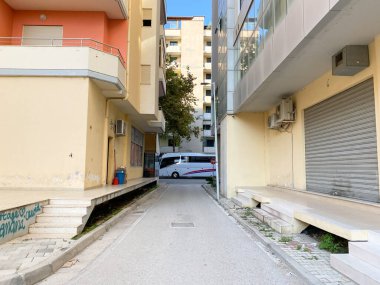 Arnavutluk 'un Vlora kenti - 16 Ocak 2025: Dar bir yol, binalar ve yeşil Akdeniz santralleriyle her gün Arnavutluk caddesi. Otantik yaşam tarzı ve bölgesel görseller için ideal.