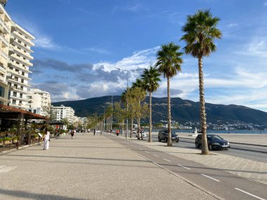 Arnavutluk 'un Vlora kenti - 16 Ocak 2025: Parlak bir gökyüzü altında palmiye ağaçları ve deniz manzaralı geniş bir Akdeniz yolu. Yaz atmosferi için kavramsal fotoğraf, tatil beldesi seyahati ve huzurlu kıyı yaşamı..