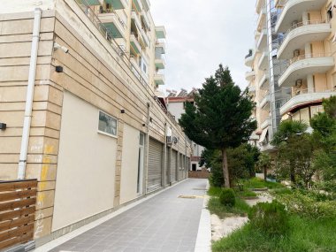 Vlora, Arnavutluk - 16 Ocak 2025: Mimari, asfalt ve yoğun yeşilliğe sahip tipik Arnavut caddesi. Yerel hayatı tasvir etmek ya da planına güney cazibesini eklemek için mükemmel..