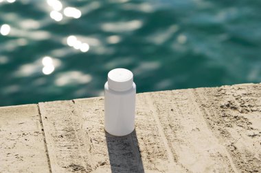 Sahildeki taşların üzerinde arka planda deniz olan beyaz bir ilaç şişesi. Doğal tıp, ilaç, sağlık desteği, organik sağlık ve bütünsel bakım kavramı.