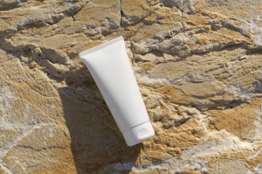 Deniz kenarındaki taşların beyaz kozmetik tüpleri. Vücut losyonunu, kremi, yüz bakımını veya doğal, kıyı estetiğine sahip organik güzellik ürünlerini desteklemek için mükemmel..